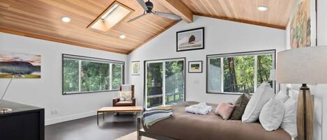 A modern bedroom with a bed, a desk, a chair, and large windows.