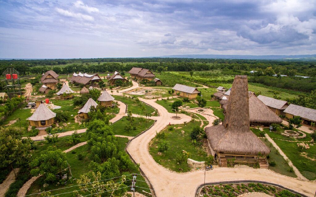 A rural village with thatched-roof houses arranged around a central path, surrounded by greenery.