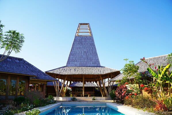 Un resort con piscina, construcciones de madera y plantas tropicales.