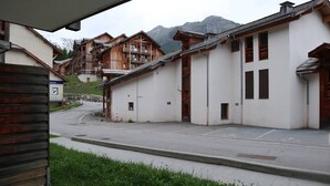 A street view with traditional wooden buildings, a white building with a garage, and a mountain in the background. - Studio Résidence LE Parc DES Airelles (LES ORRES 1800)