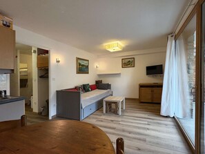 A compact living space with a kitchenette, a dining area, a sofa bed, and a television.