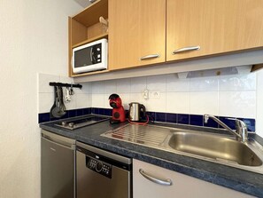 A compact kitchen with a dishwasher, a microwave, a kettle, and a sink.