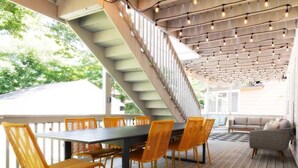 An outdoor deck with a wooden table and chairs, a staircase, and string lights. - 5BR Game Room Near Cleveland Clinic (Cleveland Heights)