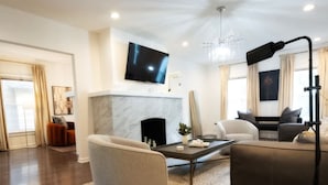 A modern living room with a fireplace, a flat-screen TV, and a large window with curtains. - 5BR Game Room Near Cleveland Clinic (Cleveland Heights)