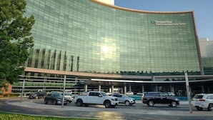 A modern building with a glass facade, a parking lot with several vehicles, and a clear sky. - 5BR Game Room Near Cleveland Clinic (Cleveland Heights)