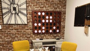 A round glass table with four yellow chairs, a brick wall, a clock, and a bulletin board. - Chic Retreat: Your Cozy Getaway with Waffles too! (Orem)