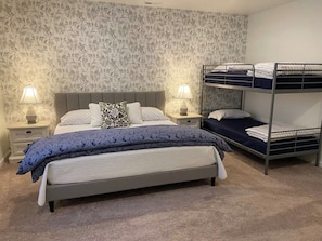 A bedroom with a bed, two bedside tables, a bunk bed, and patterned wallpaper.
