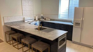 A kitchen with a marble island, bar stools, a built-in oven, and a refrigerator. - Chic Retreat: Your Cozy Getaway with Waffles too! (Orem)