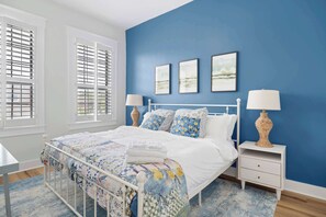 A bedroom with a bed, bedside tables, a window with shutters, and a blue wall.