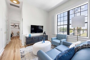 Ein modernes Wohnzimmer mit großem Fenster, Flachbildfernseher, Sofa und Couchtisch.