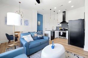 A modern living room with a blue sofa, a round coffee table, and a dining area with chairs and a table.