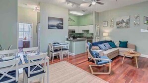 A living room with a sofa, chairs, a coffee table, and a dining area with chairs and a table. - 6x Gamer Themed 2BR Apts - Close to Stadium! (Jacksonville)