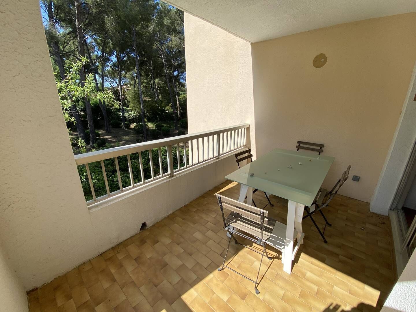 A balcony with a table and chairs, a view of trees, and a white railing.