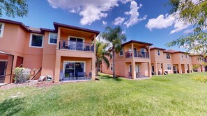 A row of two-story buildings with balconies, a grassy lawn, and a clear blue sky. - PERFECT, NEW! 6 Min to Dis, On Lake, Brand Name Beds, Big  T.Vs, Steps to Pool.  (Kissimmee)
