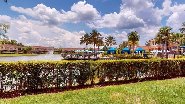 A waterfront hotel with a bridge, palm trees, and blue umbrellas. - PERFECT, NEW! 6 Min to Dis, On Lake, Brand Name Beds, Big  T.Vs, Steps to Pool.  (Kissimmee)