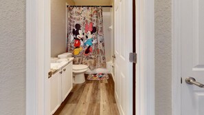 A bathroom with a Mickey Mouse and Minnie Mouse shower curtain, a toilet, and a wooden floor. - PERFECT, NEW! 6 Min to Dis, On Lake, Brand Name Beds, Big  T.Vs, Steps to Pool.  (Kissimmee)