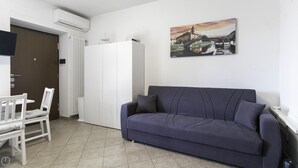 A room with a dark blue sofa, a white radiator, a white wardrobe, and a painting of a cityscape on the wall. - Italianway - Andrea Ponti 1 (Milan)