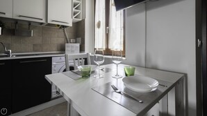 A modern kitchen with white cabinets, a built-in dishwasher, and a dining area with a table set for two. - Italianway - Andrea Ponti 1 (Milan)