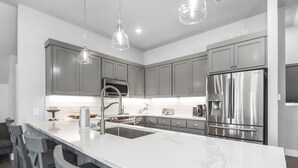 A modern kitchen with grey cabinets, stainless steel appliances, and a marble island. - Sugar Sand Cottage A (Port St. Joe)