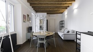 A modern living room with a wooden ceiling, a round dining table with chairs, a grey sofa, and a black bookshelf. - Italianway Comfort - Alfieri 18 (Milan)