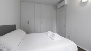 A bedroom with a bed, white curtains, a wardrobe, and an air conditioning unit. - Italianway Comfort - Alfieri 18 (Milan)