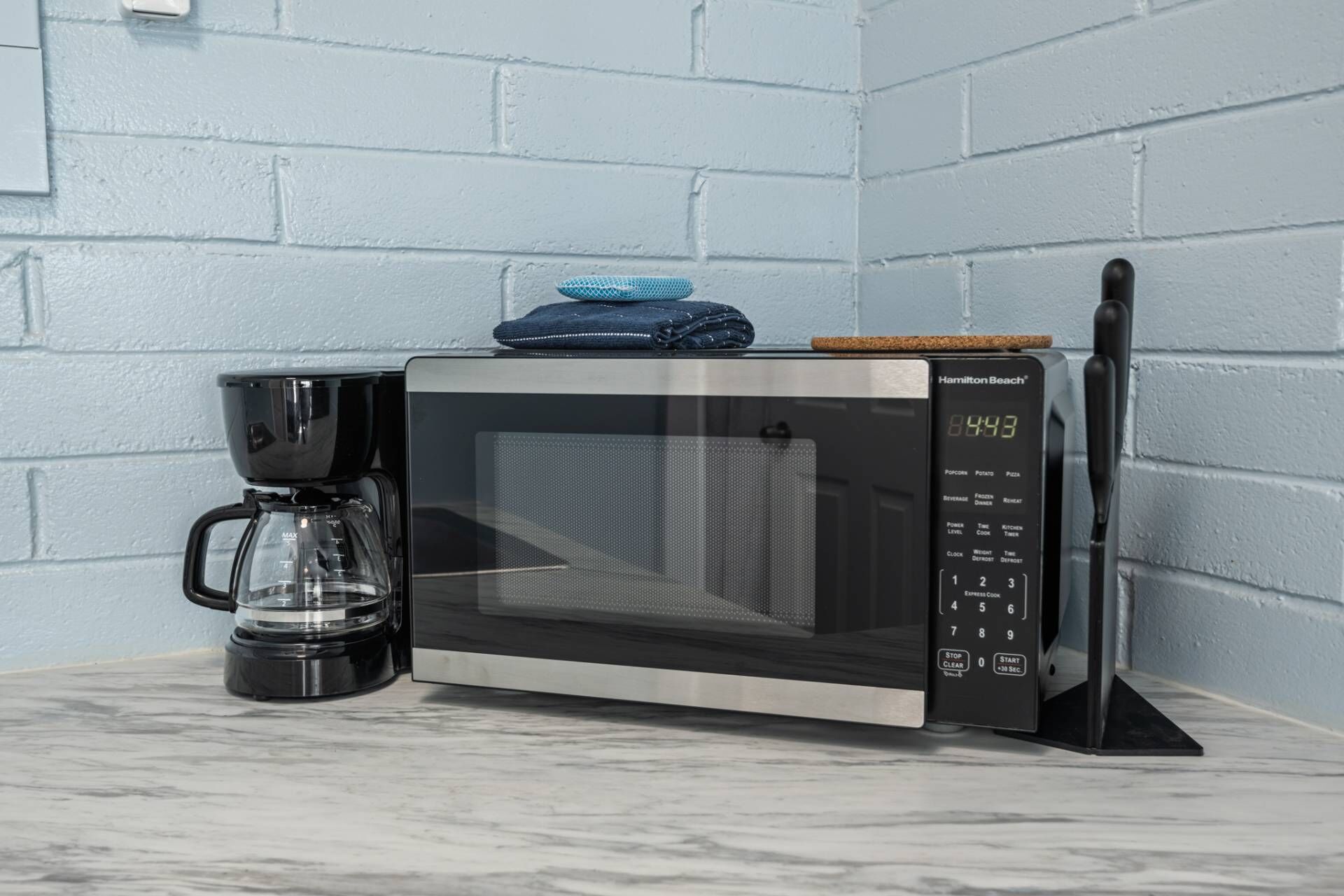 Un four à micro-ondes doté d’un écran numérique, une machine à café et un couteau, le tout posé sur un plan de travail.