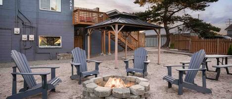 A backyard with a fire pit, four Adirondack chairs, and a wooden deck.