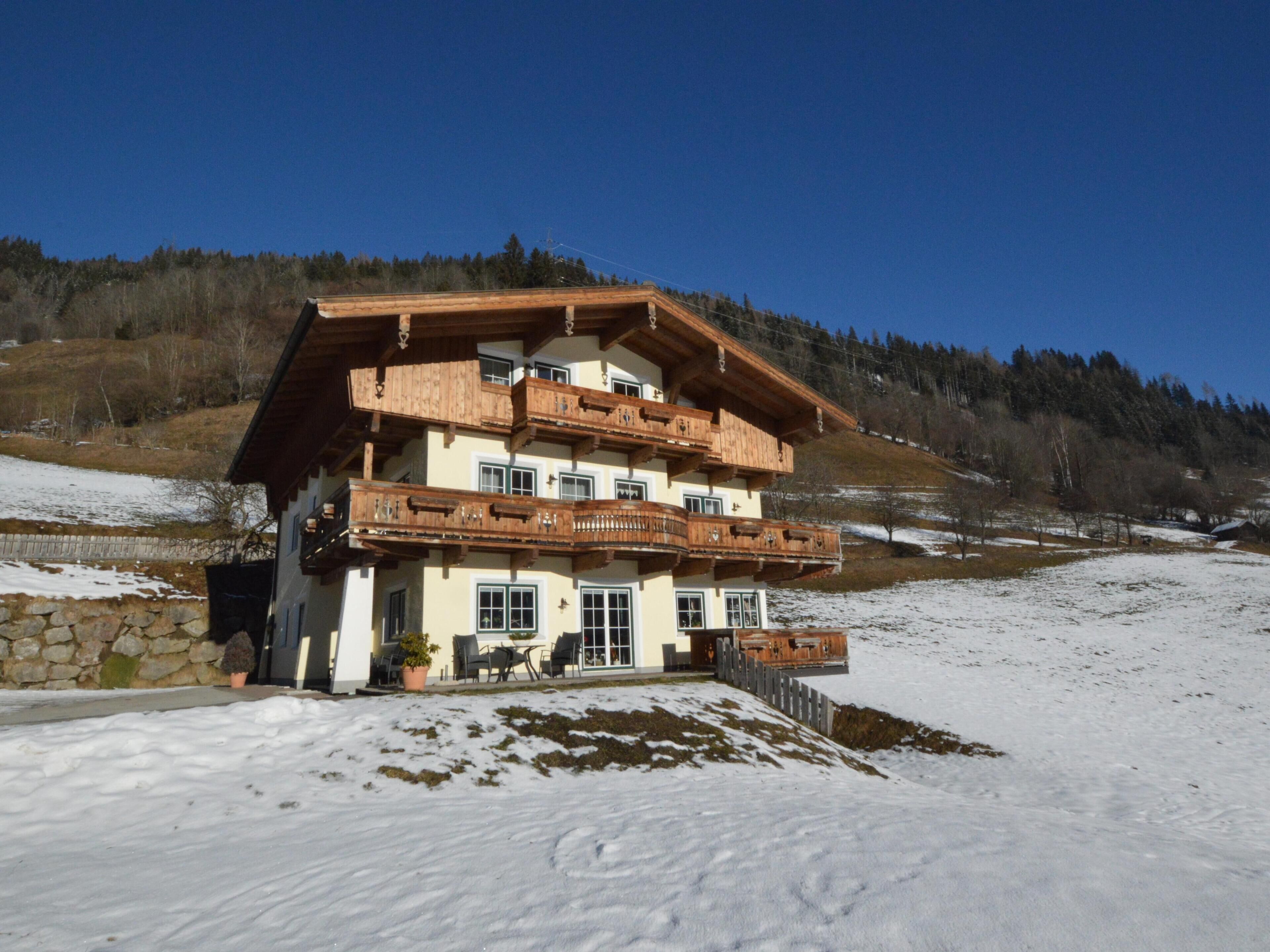 Un chalet à plusieurs étages, doté de balcons en bois, de fondations en pierre et surplombant un paysage enneigé.