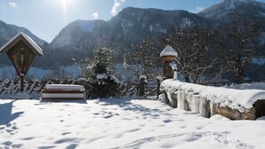 Schneebedeckte Landschaft mit Holzbauten, einer Bank und einem Zaun.