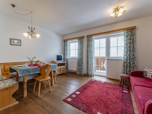 Una sala de estar acogedora con comedor, muebles de madera, una alfombra roja y un ventanal con cortinas.