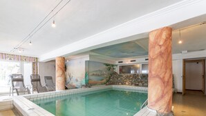 Ein Innenpool mit Wandgemälde, zwei Liegestühlen und einer Steinwand.