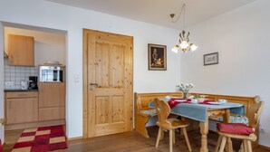 Eine kleine Küche mit Holdekor, einschließlich Küchenschränken und Backofen, ein Essbereich mit Holztisch und -stühlen sowie eine Holztür.