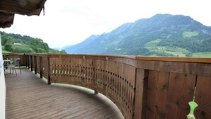 Eine Holzterrasse mit gewölbter Brüstung, die auf eine gebirgige Landschaft blickt.