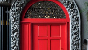 Une porte rouge surmontée d’une arche décorative et d’une grille en métal.