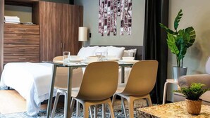 Une chambre d’hôtel moderne comprenant un lit, un coin repas avec des chaises, une table, une plante et un mur décoré de photos.