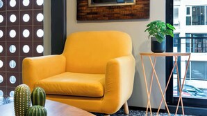 Una habitación moderna con un sillón amarillo, una mesita de centro de madera, una planta en maceta y un espejo grande en la pared.