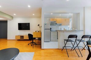 A modern living room with a flat-screen TV, a wooden desk, and a dining area with chairs.