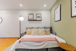 A bedroom with a bed, pillows, a bedside table, a lamp, and wall art.