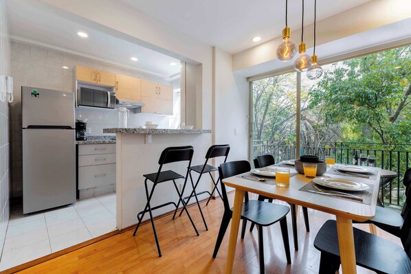 A modern kitchen with a refrigerator, microwave, and dining area with chairs and a table set for two.