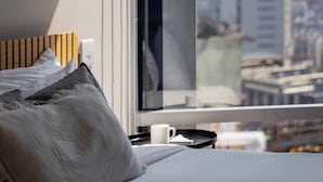 Una habitación de hotel con cama, ventana con vista a la ciudad y un cuadro en la pared.