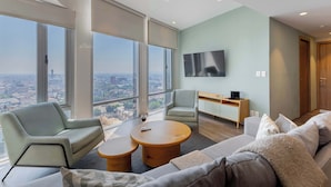 Una sala de estar moderna con un sofá, dos sillones, una mesa de centro, un televisor de pantalla plana y vistas a la ciudad.