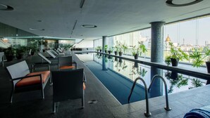 A modern indoor pool area with seating and potted plants, large windows offering city views. - Capitalia | Refined Duplex | Full Gym & Security (Ciudad de México)
