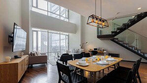 A spacious dining area with a high ceiling, large windows, and a staircase leading to an upper level. - Capitalia | Refined Duplex | Full Gym & Security (Ciudad de México)