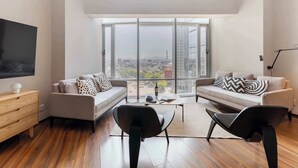 A modern living room with a large window, a sofa set, a coffee table, and a TV on a wooden cabinet. - Capitalia | Refined Duplex | Full Gym & Security (Ciudad de México)