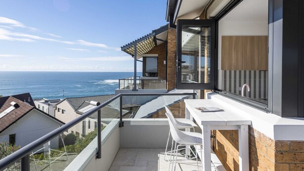 A balcony with a view of the ocean, a white table, and a chair. - Namanula 7 - Oceanstays (Yamba)