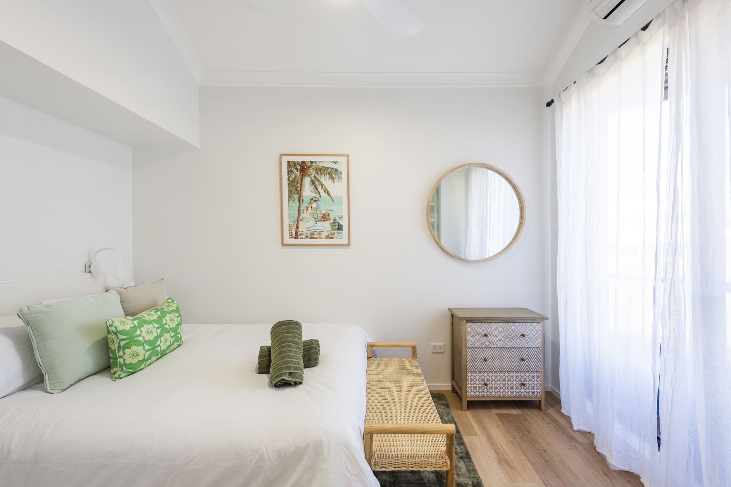 Um quarto com cama, travesseiros, mesa de cabeceira, espelho e um quadro na parede.