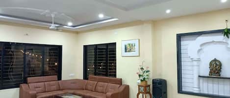 A living room with a brown sectional sofa, a coffee table, a small side table with a plant, and a large speaker.