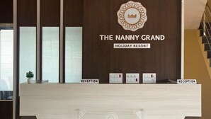 Mostrador de recepción en The Nanny Grand Holiday Resort con un diseño moderno, que incluye un ventilador de techo, un logotipo y señalización de recepción.