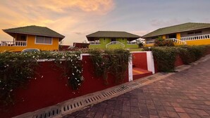 Un hilero de edificios de un solo piso y colores vivos, con un muro rojo y un camino empedrado que lleva a la entrada.