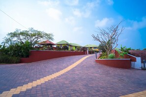 A paved pathway leading to a building with a red wall and green roof. - The Nanny Grand Resort (Malvan)